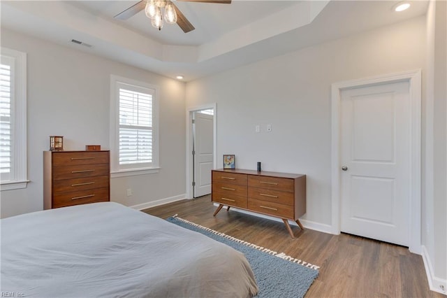 bedroom with recessed lighting, wood finished floors, visible vents, baseboards, and a raised ceiling