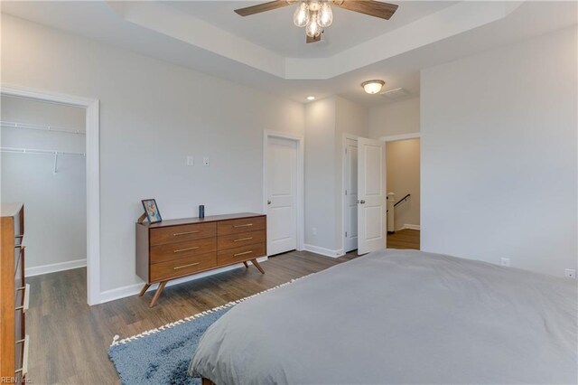 bedroom featuring a tray ceiling, dark wood-style flooring, a walk in closet, a closet, and baseboards