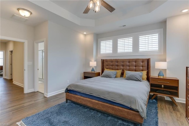 bedroom with visible vents, baseboards, a raised ceiling, and wood finished floors