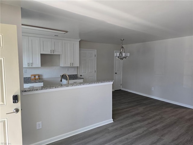 kitchen featuring dark wood finished floors, white cabinets, backsplash, a chandelier, and a sink