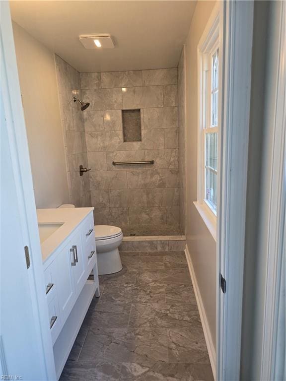 bathroom featuring toilet, a wealth of natural light, tiled shower, and vanity