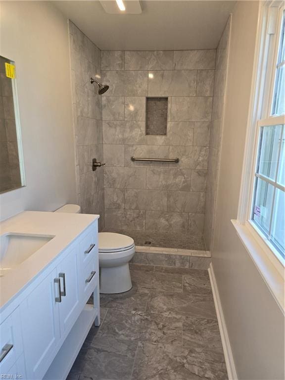 full bathroom featuring toilet, baseboards, tiled shower, and vanity