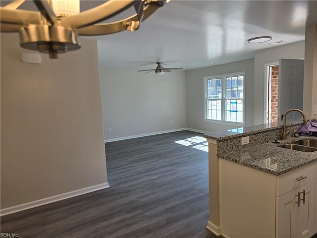 kitchen featuring light stone counters, dark wood-type flooring, white cabinets, a sink, and baseboards