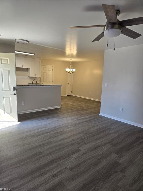 unfurnished living room with a sink, baseboards, dark wood-style flooring, and ceiling fan with notable chandelier