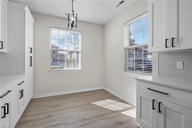 unfurnished dining area featuring light wood-style flooring, visible vents, and baseboards