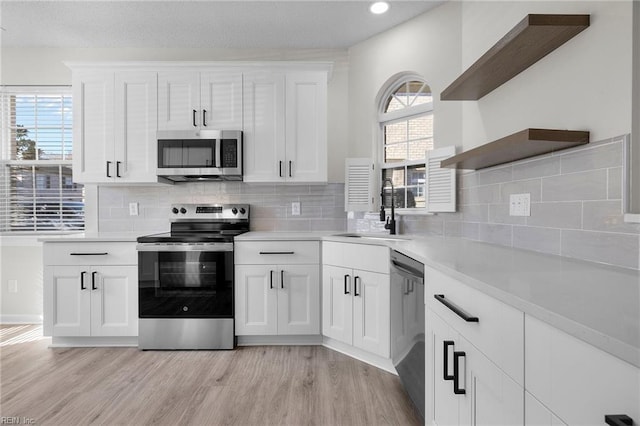 kitchen with appliances with stainless steel finishes, a sink, light wood-style flooring, and open shelves