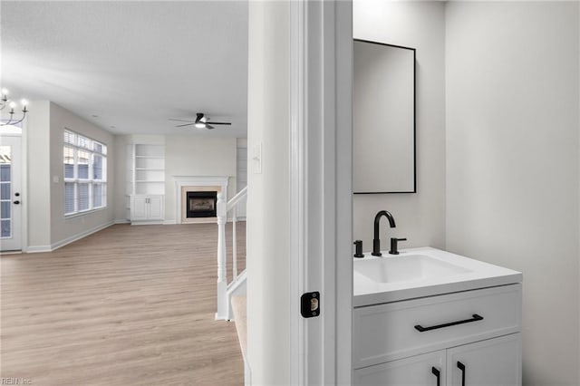 bathroom with ceiling fan with notable chandelier, a fireplace, wood finished floors, vanity, and built in features