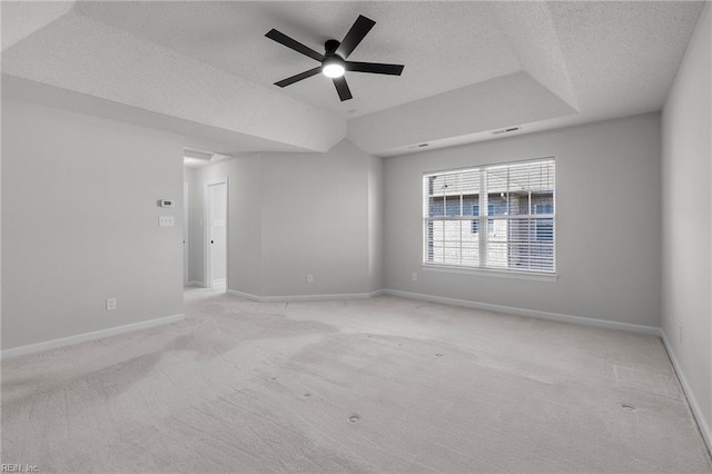 empty room featuring light carpet, a textured ceiling, a raised ceiling, and baseboards