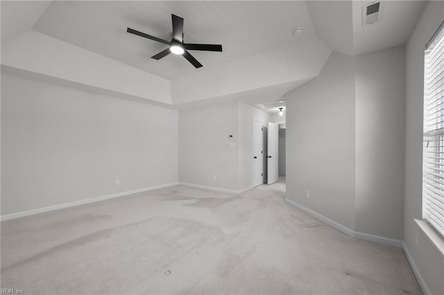 spare room featuring light carpet, visible vents, baseboards, ceiling fan, and a tray ceiling