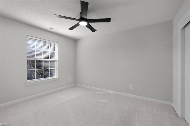 carpeted spare room with baseboards, a textured ceiling, visible vents, and a ceiling fan