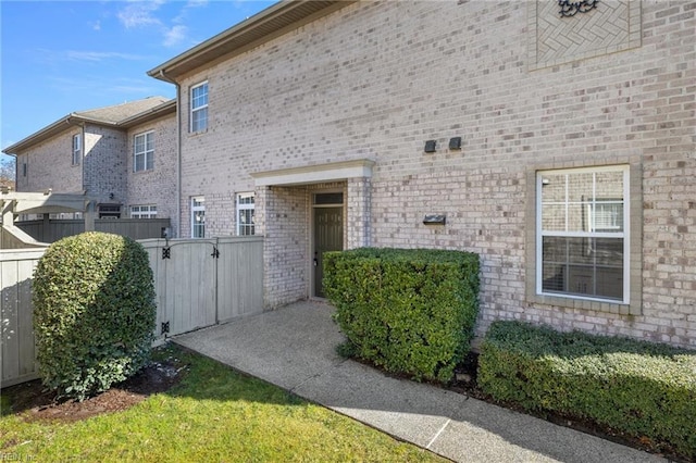 entrance to property featuring a gate, fence, and brick siding