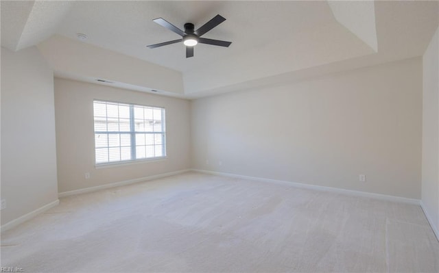 spare room featuring a tray ceiling, light colored carpet, and baseboards