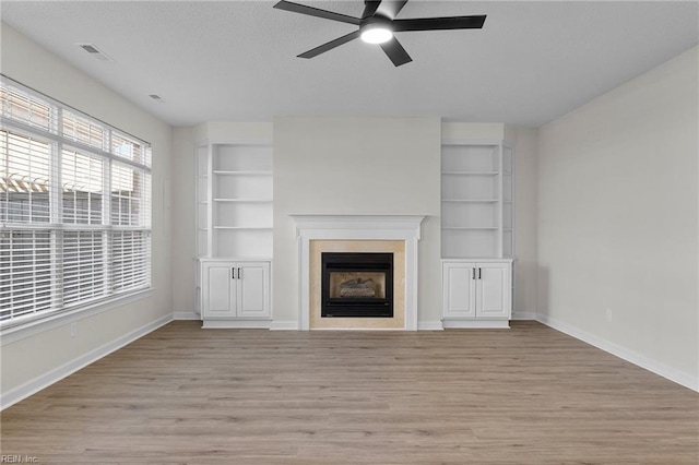 unfurnished living room with built in shelves, a fireplace, visible vents, light wood-type flooring, and baseboards