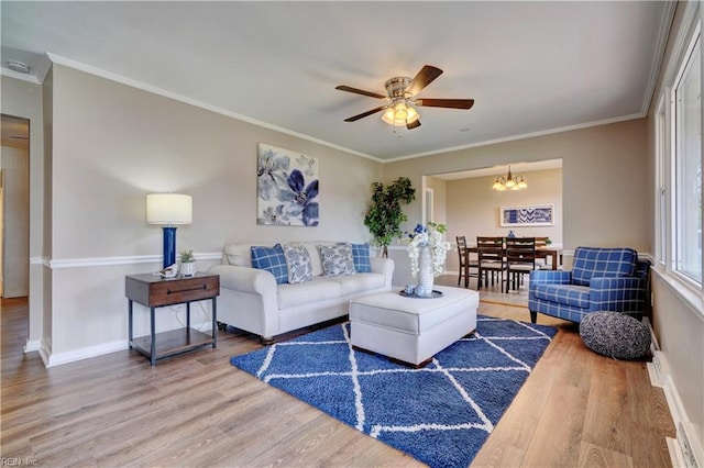 living room with ceiling fan with notable chandelier, baseboards, wood finished floors, and ornamental molding