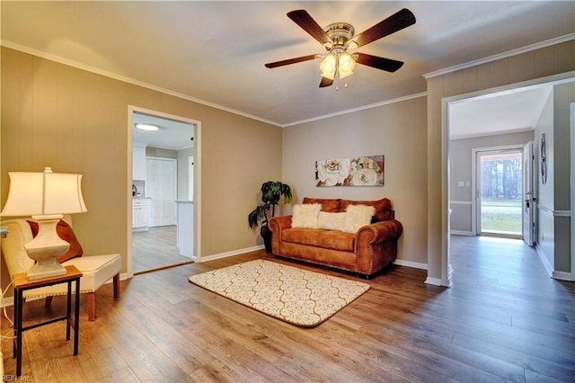 living room with a ceiling fan, crown molding, baseboards, and wood finished floors