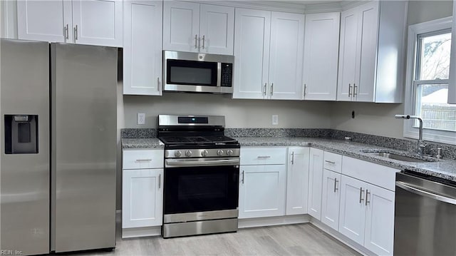 kitchen with a sink, light stone counters, appliances with stainless steel finishes, and white cabinets