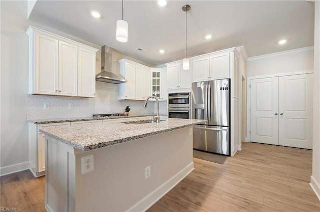 kitchen featuring wall chimney range hood, light wood-style flooring, stainless steel appliances, and a sink