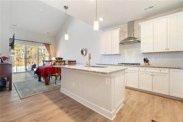 kitchen with tasteful backsplash, visible vents, light wood-style floors, wall chimney range hood, and a sink