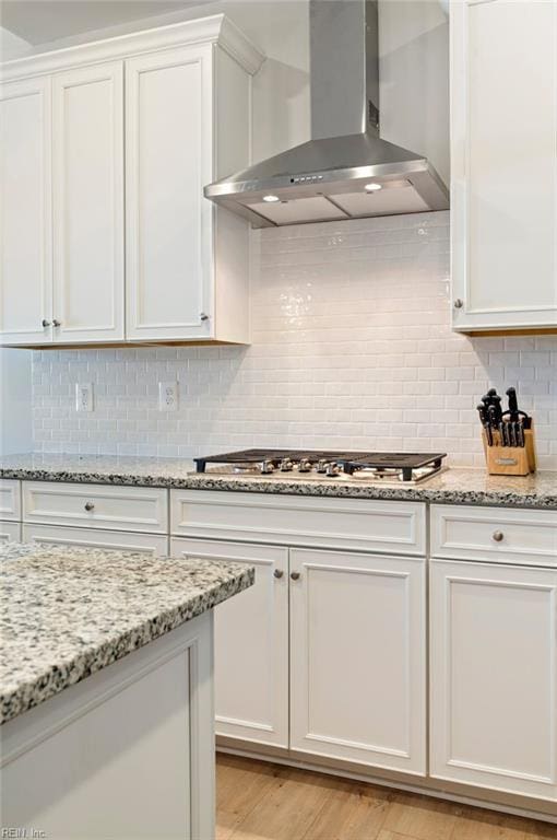 kitchen featuring tasteful backsplash, white cabinets, light stone counters, wall chimney range hood, and stainless steel gas stovetop