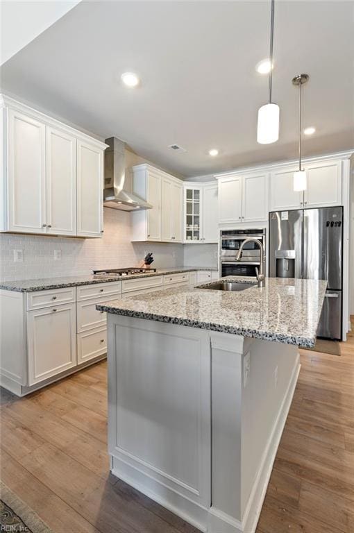 kitchen with stainless steel appliances, wall chimney range hood, a sink, and light wood-style floors