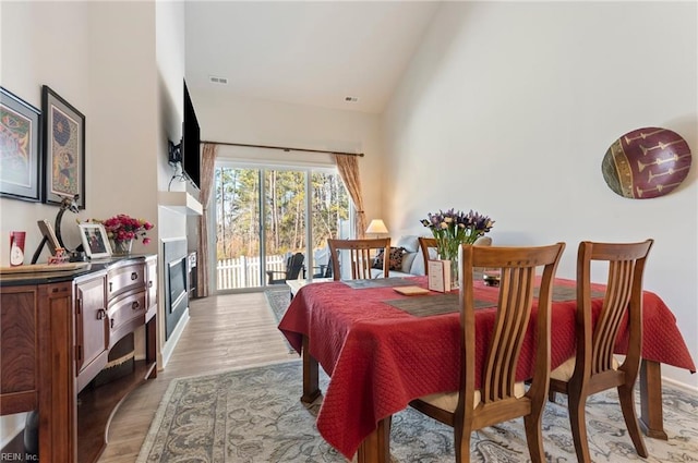 dining space featuring light wood finished floors, visible vents, and high vaulted ceiling