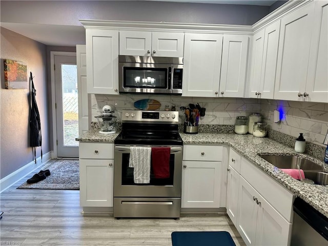 kitchen with light wood-style flooring, a sink, white cabinetry, appliances with stainless steel finishes, and tasteful backsplash