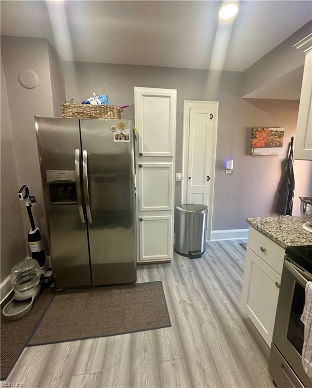 kitchen featuring light stone counters, appliances with stainless steel finishes, light wood-style floors, white cabinets, and baseboards