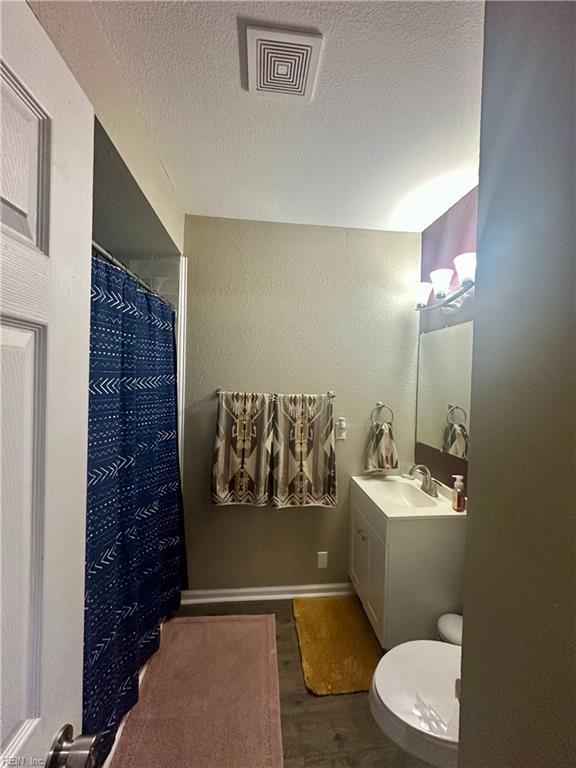 bathroom featuring a textured ceiling, toilet, wood finished floors, vanity, and visible vents