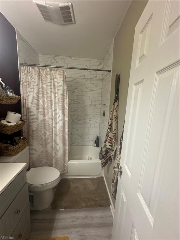 bathroom with visible vents, toilet, wood finished floors, shower / bath combination with curtain, and vanity