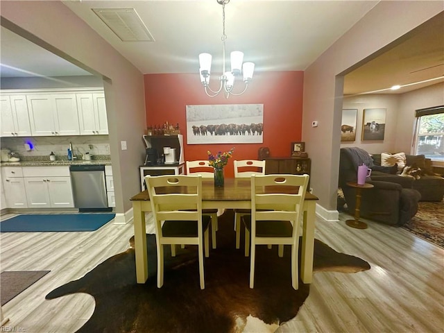 dining space featuring baseboards, light wood finished floors, visible vents, and a notable chandelier