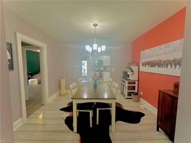 dining space with light wood-style floors, baseboards, and a notable chandelier