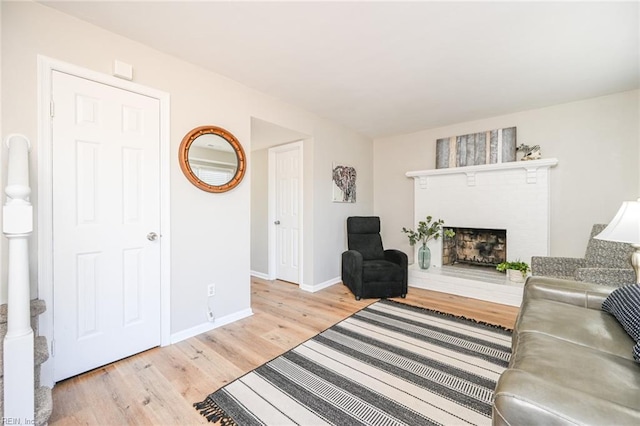 living area with a fireplace with raised hearth, light wood-style flooring, and baseboards