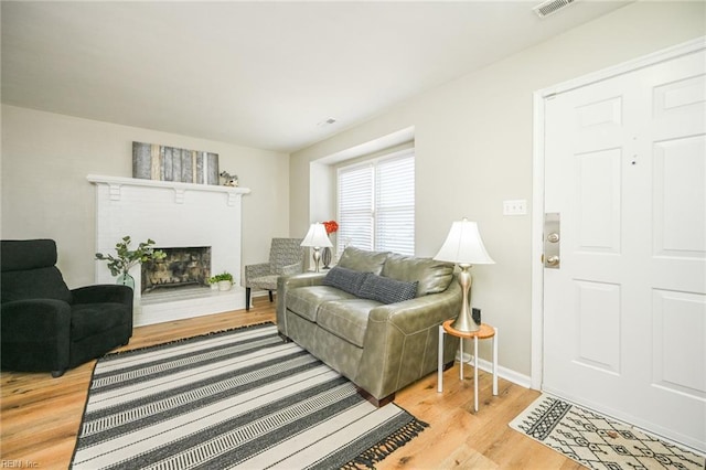 living room featuring light wood-style floors, a brick fireplace, and baseboards