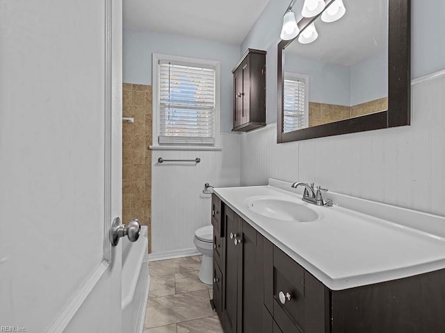 bathroom featuring toilet, a wainscoted wall, walk in shower, and vanity