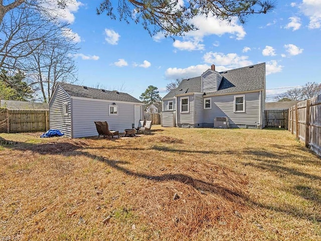 back of house featuring an outdoor fire pit, a lawn, a chimney, and a fenced backyard