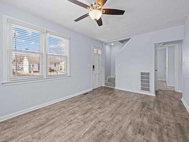 unfurnished room featuring baseboards, visible vents, a ceiling fan, stairway, and wood finished floors