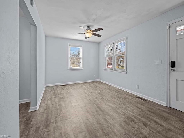 spare room featuring a ceiling fan, visible vents, baseboards, and wood finished floors