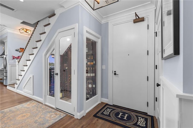foyer entrance featuring visible vents, crown molding, stairway, and wood finished floors