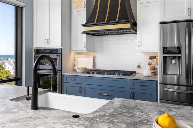 kitchen with stainless steel appliances, premium range hood, backsplash, and white cabinetry