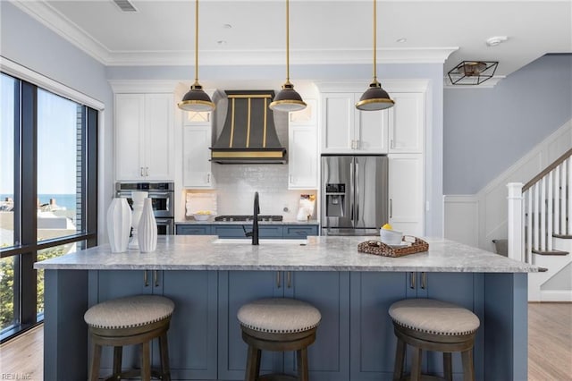 kitchen with white cabinetry, appliances with stainless steel finishes, custom exhaust hood, light wood finished floors, and crown molding