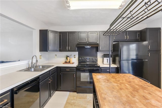 kitchen with under cabinet range hood, butcher block countertops, a sink, dark cabinetry, and black appliances