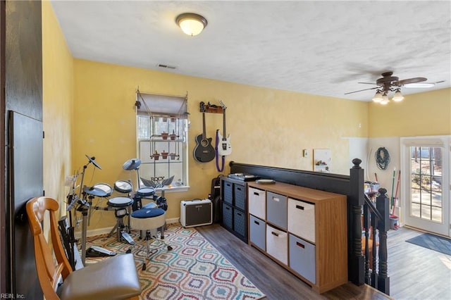 misc room with visible vents, ceiling fan, an upstairs landing, wood finished floors, and baseboards