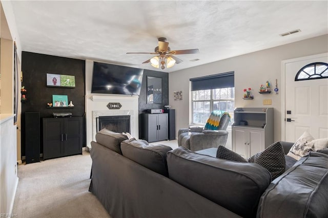 living area with a high end fireplace, visible vents, a ceiling fan, and light colored carpet