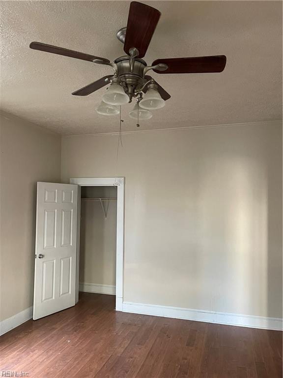 unfurnished bedroom featuring dark wood-style floors, a textured ceiling, baseboards, and a ceiling fan