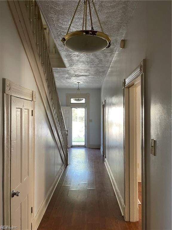 hallway with a textured ceiling, stairs, baseboards, and dark wood-style flooring