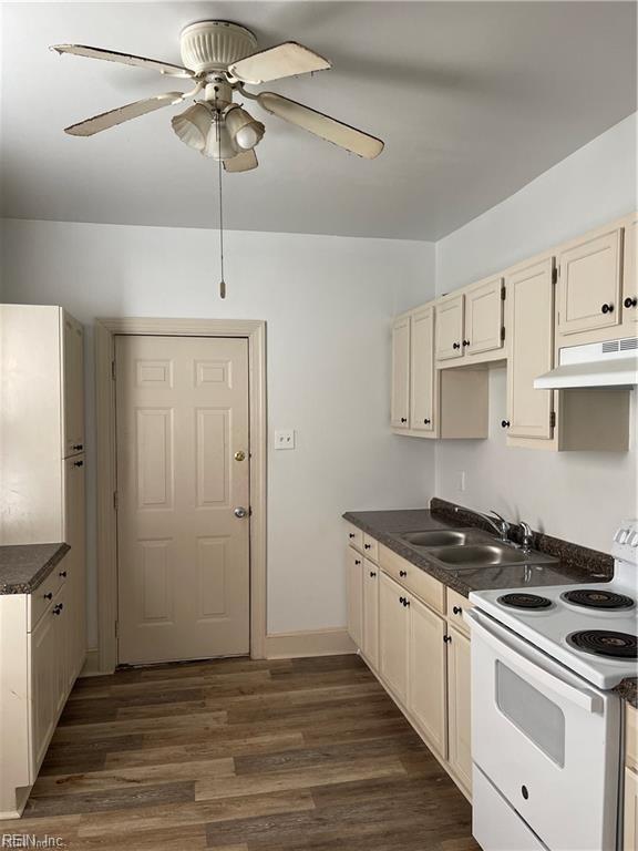 kitchen with dark wood finished floors, dark countertops, electric range, a sink, and under cabinet range hood