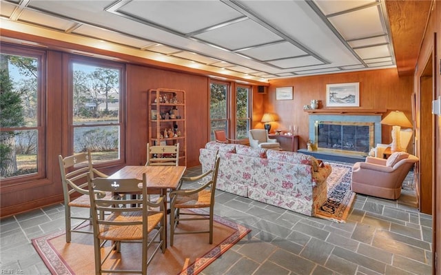 dining area with wood walls, a glass covered fireplace, and stone finish floor