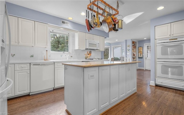 kitchen with a wealth of natural light, white appliances, visible vents, and white cabinets