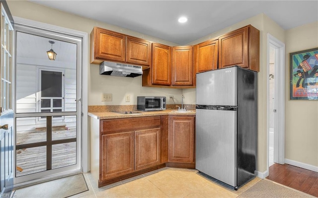 kitchen with baseboards, brown cabinetry, stainless steel appliances, light countertops, and under cabinet range hood