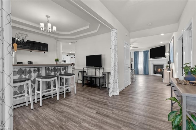 kitchen featuring a tray ceiling, a glass covered fireplace, open floor plan, wood finished floors, and ceiling fan with notable chandelier